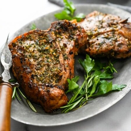 Grilled pork chops garnished with fresh herbs on a silver platter, showcasing a juicy and flavorful meal perfect for dinner.